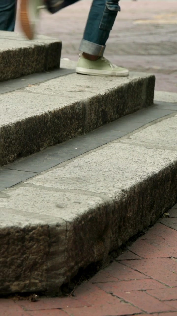 Vertical video: Walking man nearing steps on brick path, bike passing, then going up with brown bag