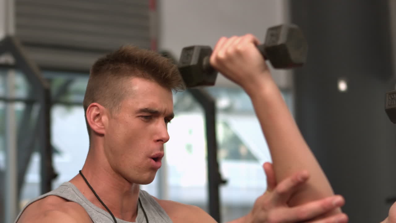 매력적인 건강한 여성이 코치와 함께 덤벨을 들어 올리고 있습니다.