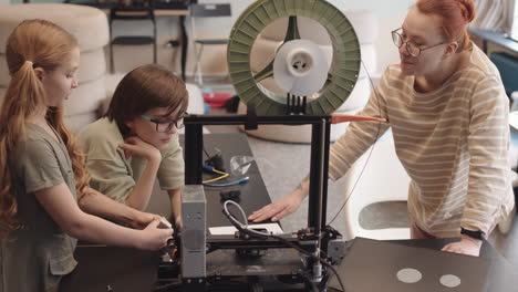 teacher and two teenagers watching 3d printer working