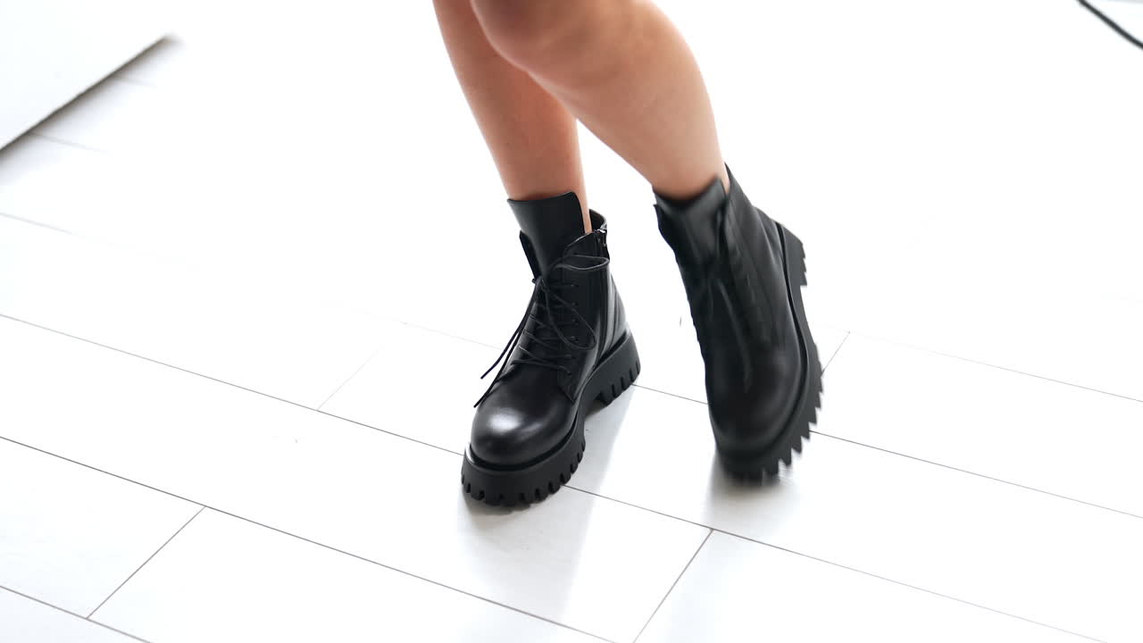 Model showing the elegant black leather low boots with tractor soles. Fashionable footwear show at white floor backdrop. Top view.