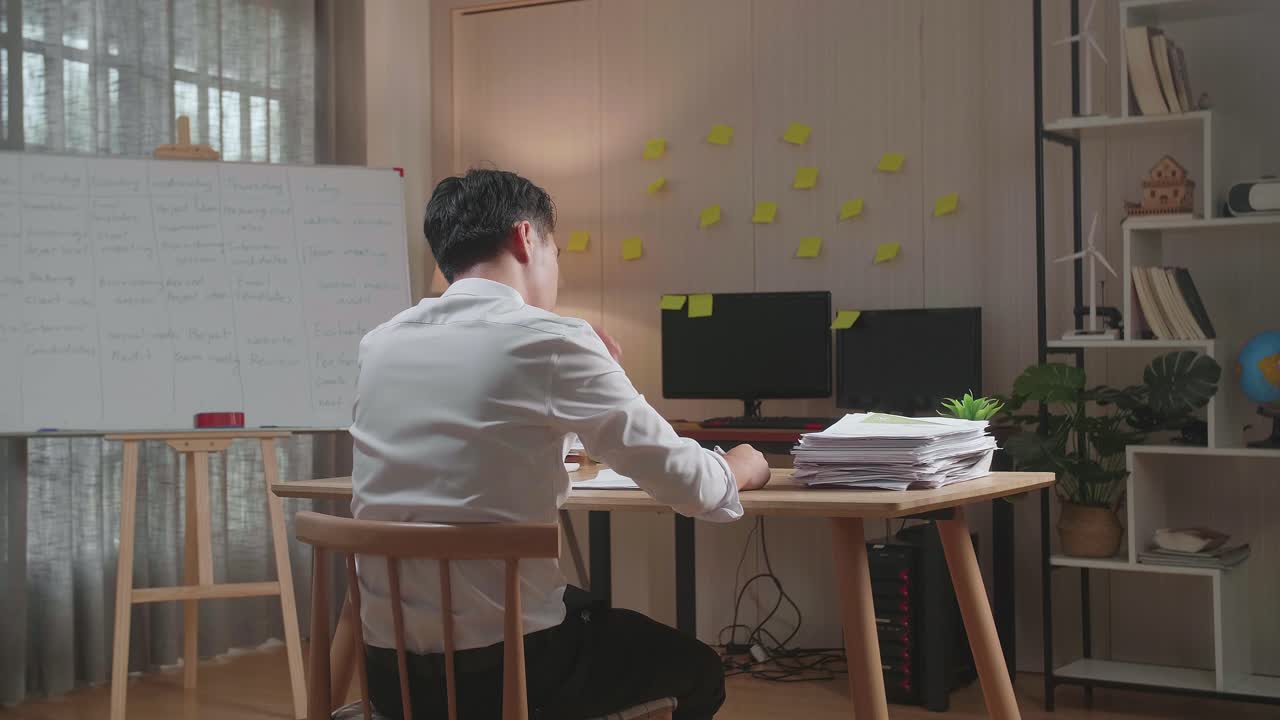 vista trasera de un hombre asiático con dolor de cabeza mientras trabaja duro con documentos en la oficina