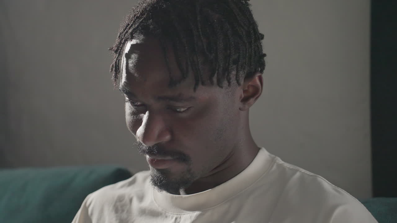 Champ sitting comfortably on teal sofa, focused on tablet with deep concentration. Soft sunlight highlights his face, creating a peaceful, reflective moment in a cozy, modern living room
