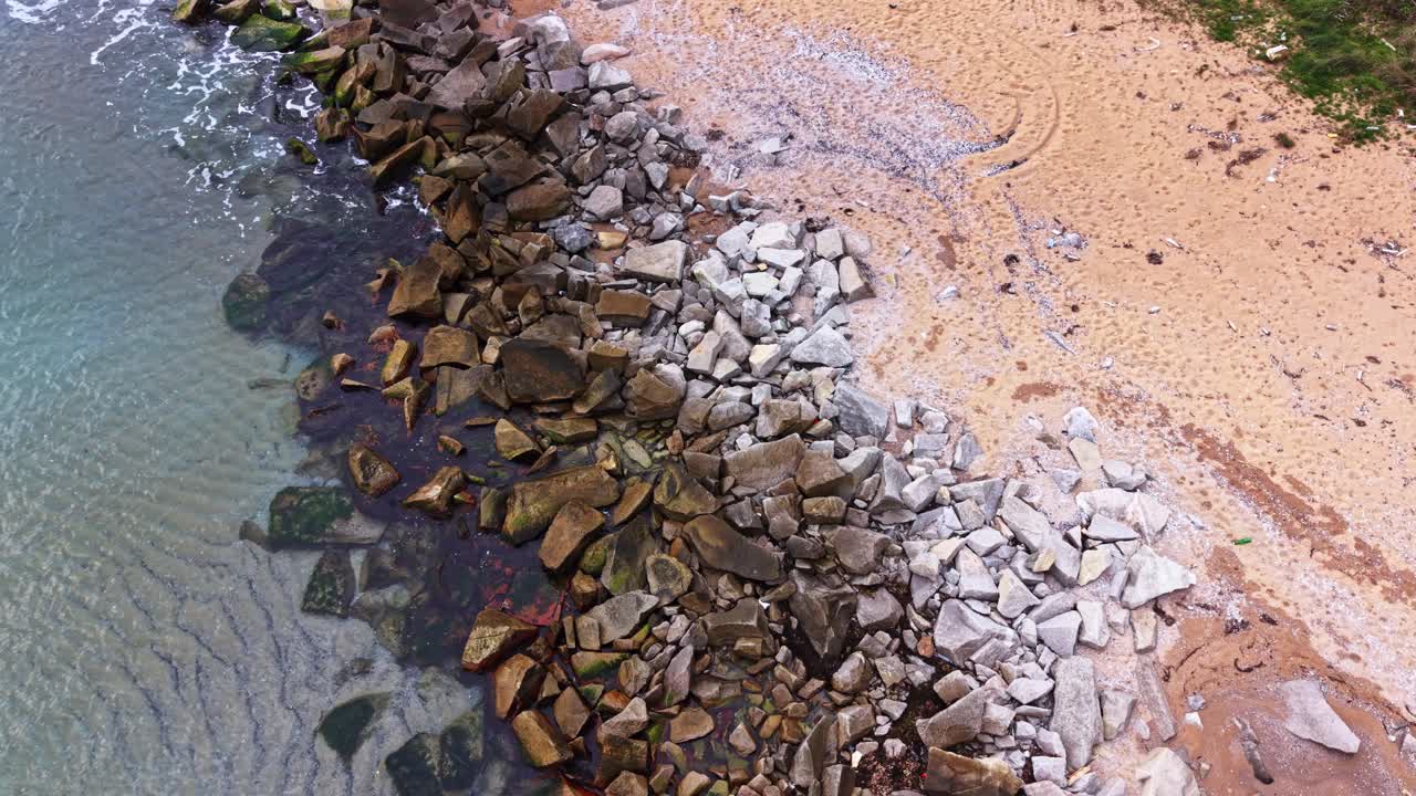 Rocky shore with sand beach and calm water in aerial view