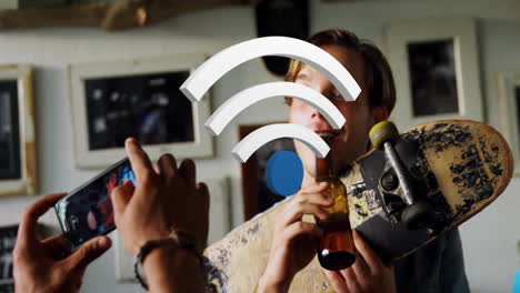 Two men holding skateboard and bottle using smartphone for tech shoot featuring floating Wi?Fi icon
