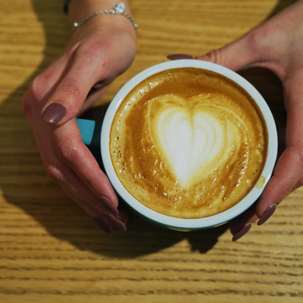 Cup with coffee on wooden background. Latte art of heart design on coffee. Female hands taking cup of hot drink from the wooden surface. Top view.