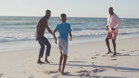 Video-Eines-Glücklichen-Afroamerikanischen-Großvaters,-Vaters-Und-Sohnes,-Der-Am-Strand-Fußball-Spielt