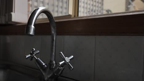 metallic silver tap dripping then leaking slowly in traditional home kitchen sink with hot and cold taps