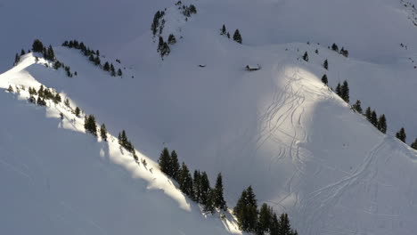 aerial view, flying up a snowy valley towards a mountain hut in the french alps in winter with boring light