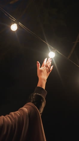 mujer empuja guirnalda de luces en glamping contra el bosque. joven esposa disfruta de la tranquilidad de la noche entre el bosque iluminado tarde en la noche. explorando las cercanías del campamento