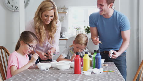 parents with children sitting at table decorating eggs for easter at home