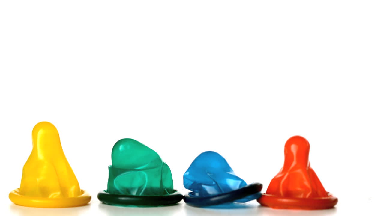 cuatro condones de colores cayendo sobre un fondo blanco