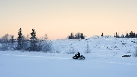 seguimiento aéreo de un hombre conduciendo motos de nieve en un desierto remoto en canadá