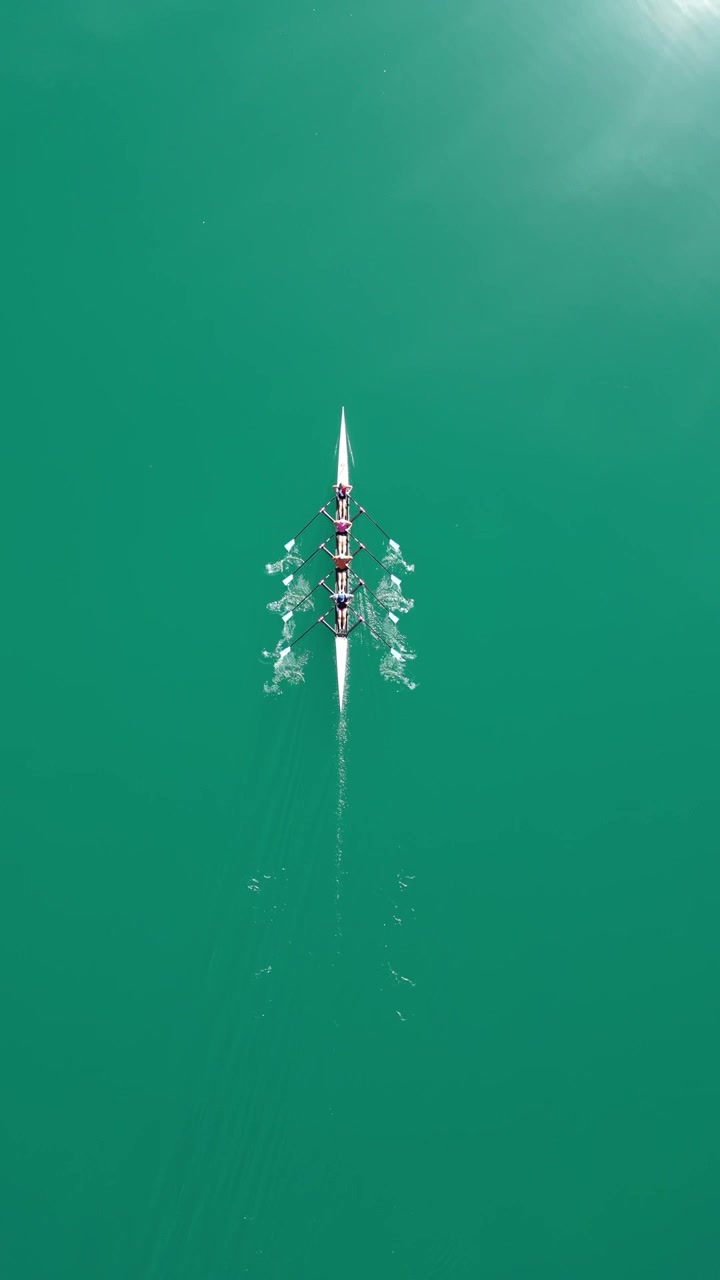 Four-person rowing team training on vibrant turquoise water watersport, top down vertical video