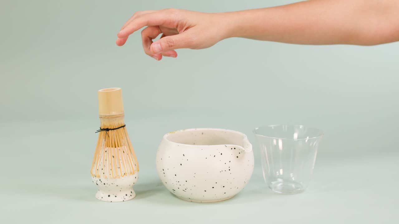 Hand whisks matcha tea in ceramic bowl with bamboo whisk, minimal background, soft lighting
