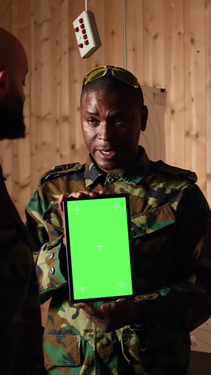 Vertical video Soldiers watching instructional videos on green screen tablet shown by commander