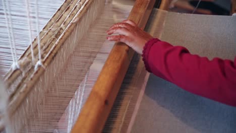 Hands-of-elder-person-weaving-with-antique-wooden-machine,-close-up-view