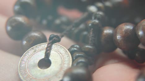 a wooden beads necklace with an old asian coin in a man hand, macro shot, 4k