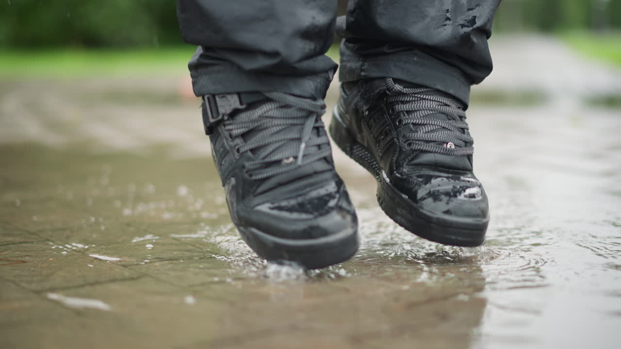 Mujer pisando un charco en la ciudad, botas mojadas encontrándose con el pavimento de baldosas con suaves salpicaduras, reflejos borrosos del horizonte en la superficie, pausa de un viajero apresurado y paso pensativo, pantalones y cordones húmedos