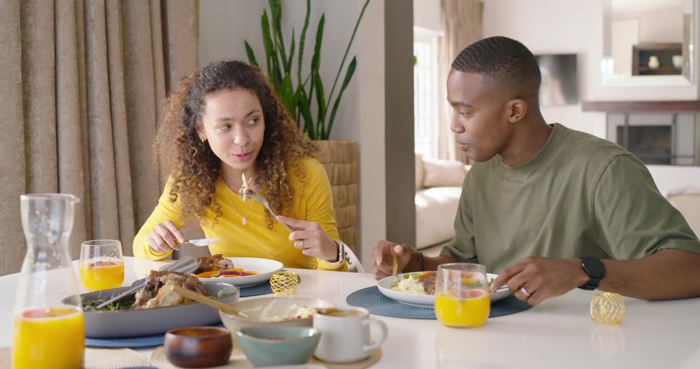 Hispanic woman yellow cutting food African-American man after sipping orange juice leaning talking
