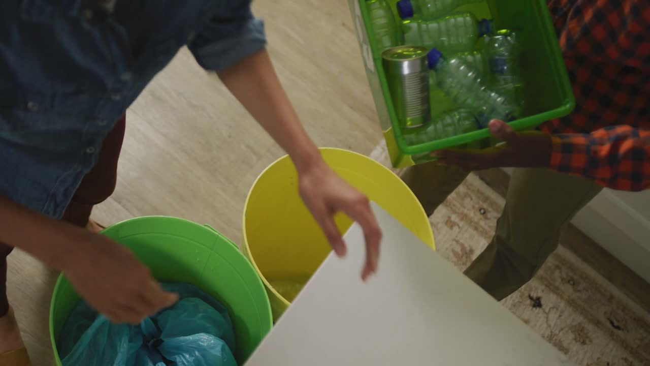 pareja diversa con camisa y chaqueta segregando residuos en la cocina
