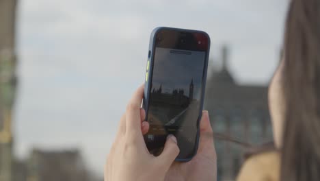 primer plano de una mujer de vacaciones tomando fotos de las casas del parlamento en londres reino unido en el teléfono móvil