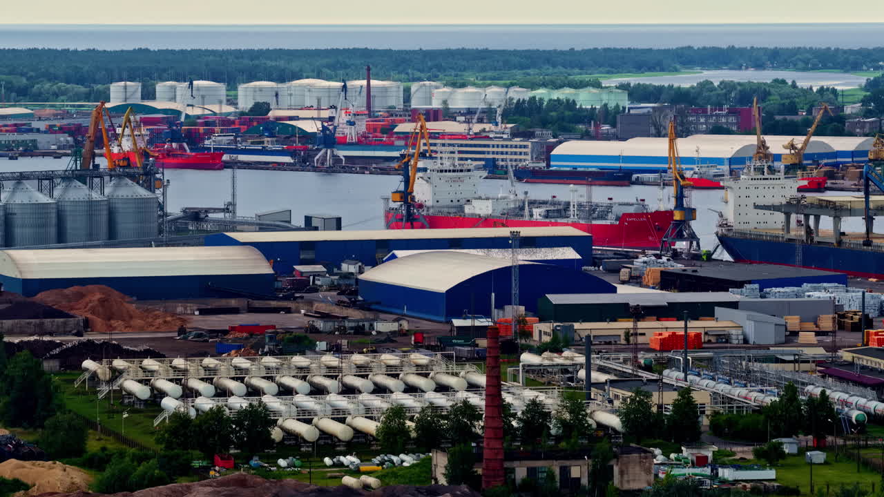 A wide aerial view captures the vast industrial complex of the Port of Riga, including KS Terminal, a propane gas export base, docked cargo ships, cranes, and numerous storage facilities