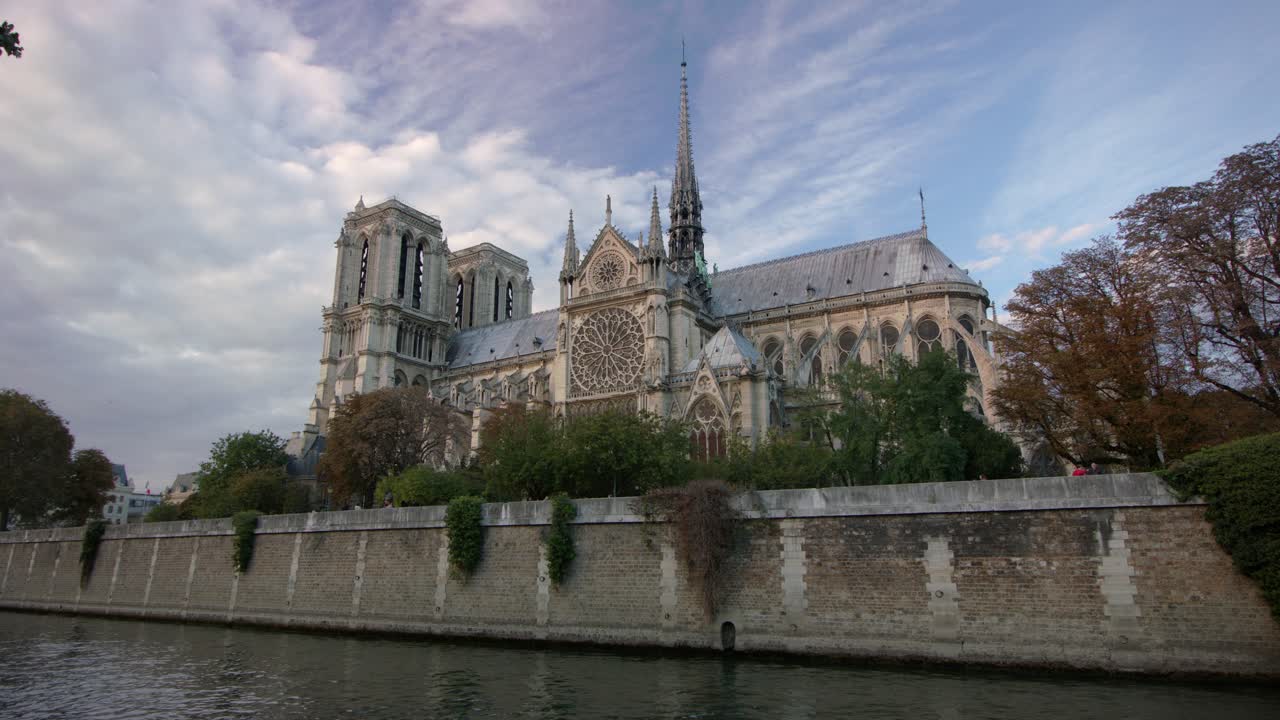 Notre Dame Katedrali, Seine Nehri üzerinde yükselirken, Gotik mimarili detaylı cephesi ve nehir kenarındaki ağaçlarla birlikte yumuşak öğleden sonra ışığı altında ikonik bir Paris şehir sahnesi yaratıyor