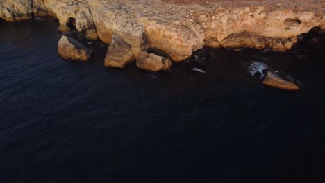 Drone-top-down-aerial-view-of-waves-splash-against-rocky-seashore,-background