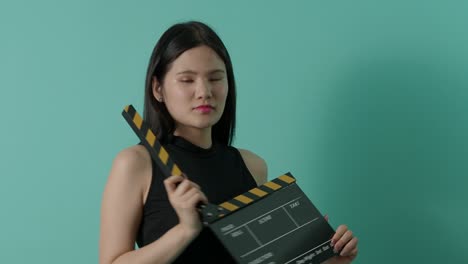 movie slate and little sexy cute asian girl. woman holding and clapping movie clapperboard or film slate with green screen background. camera zooming in and out to show her smile. video production.