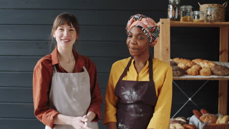 portrait of two cheerful multiethnic colleagues making dough in bakery