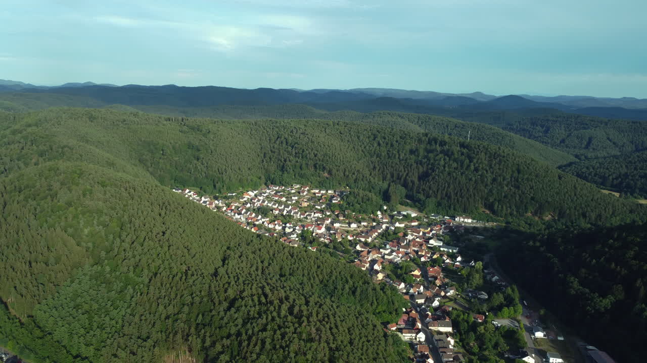 Aerial view of a village nestled in a valley surrounded by forest and mountains