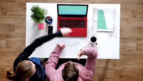 joven con gafas y mujer mirando en la computadora portátil, aclamando y dando los cinco altos, topshot, escritorio con café y documentos