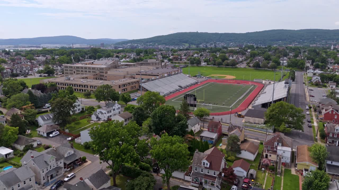 Aerial flyover Bethlehem city in Pennsylvania with traffic on streets. Liberty High School and BASD stadium in distance. Sunny day in summer. Wide shot
