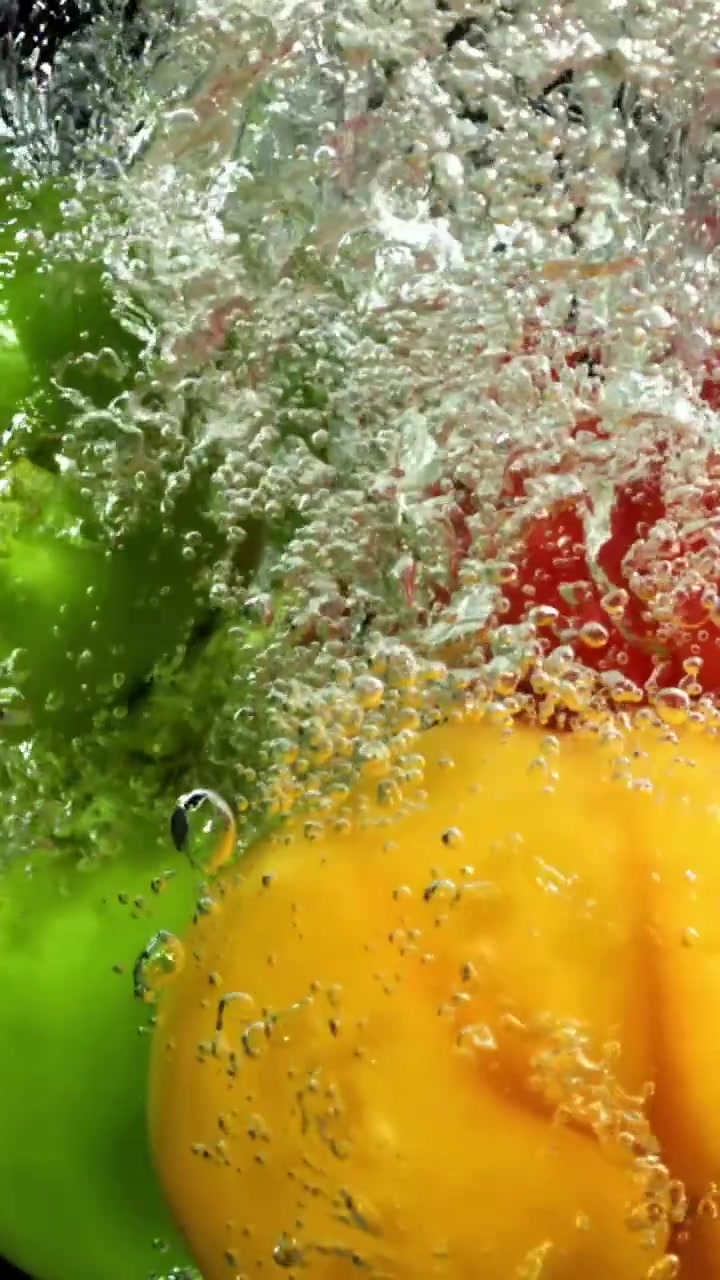 Bunte Paprikaschoten platschen in Zeitlupe ins Wasser