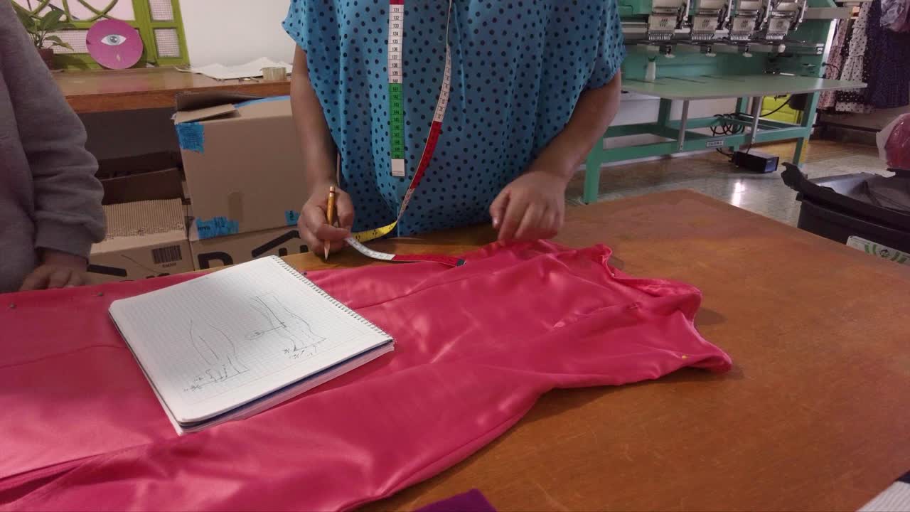 diseñadora de moda latina midiendo un vestido en una mesa de madera tomando notas