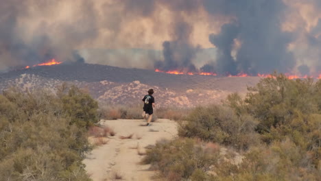 a teenager, child runs up hill to watch enormous wildfire burn, tall black billows of smoke rise