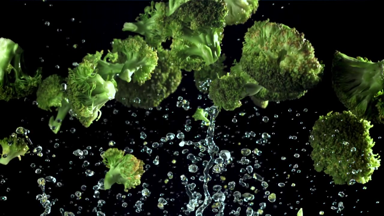 Cimette di broccoli verdi freschi che cadono con schizzi d'acqua al rallentatore