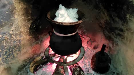 moroccan couscous cooking on a couscoussier steamer to steam it
on a wooden fire in a fireplace, smoke and flame surround the pot-1