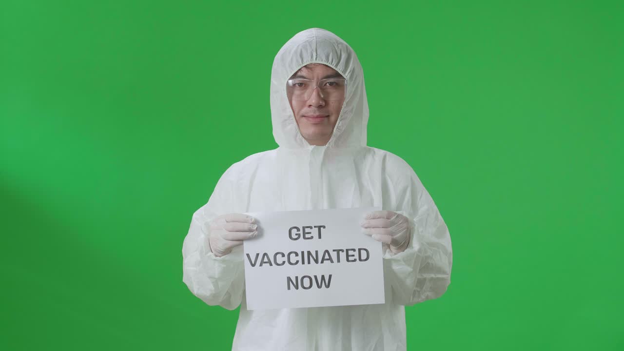 Asian Man Wearing Personal Protective Equipment Uniform Ppe And Holding Get Vaccinated Now Sign In The Green Screen Studio