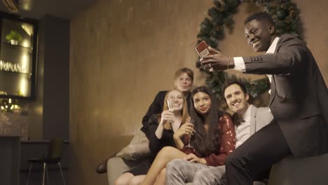 group of friends dressed in elegant clothes enjoying new year's party. they're sitting on the couch taking a selfie