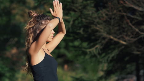 young woman meditating through yoga pose at hill