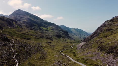 Impresionante-Vista-Aérea-De-La-Carretera-Que-Atraviesa-El-Valle-En-Snowdonia-Gales,-Con-El-Coche-Conduciendo-Hacia-Snowden