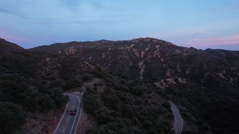 aerial view of black car driving along mountain pass at sunset, road trip along mountainside roadway