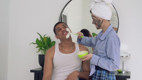 female applying facial mask to a handsome black man