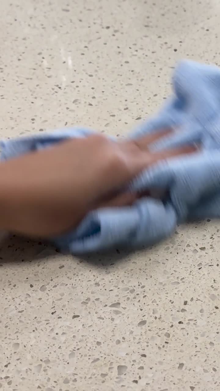 Hand using a blue microfiber cloth to wipe a brown liquid spill from a countertop