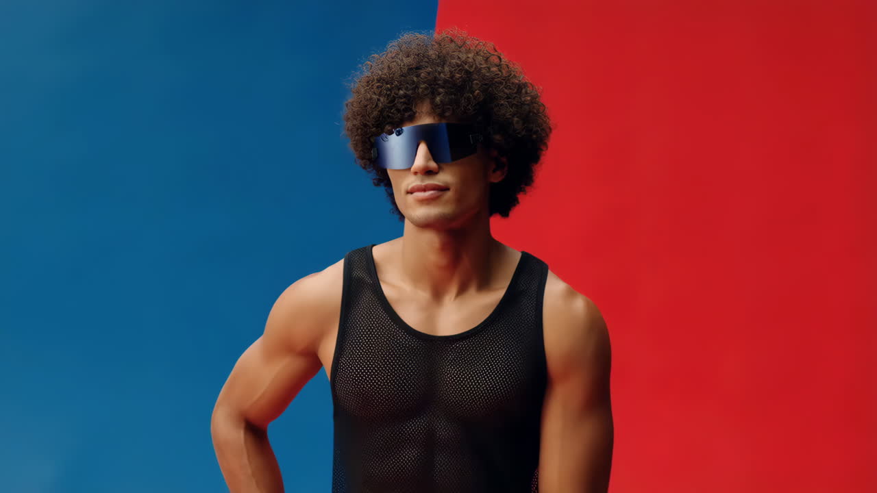 Man with curly hair and futuristic sunglasses against a red and blue background