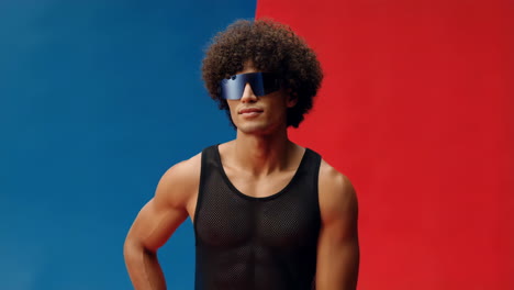 man with curly hair and futuristic sunglasses against a red and blue background
