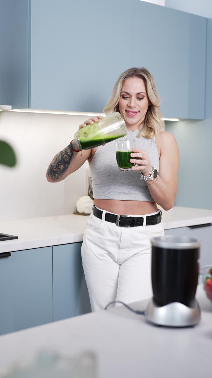 Vertical - Cheerful Woman In Kitchen Pouring Prepared Smoothie Into Glass. medium shot