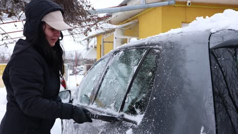 woman cleaning car from snow after blizzard - closeup