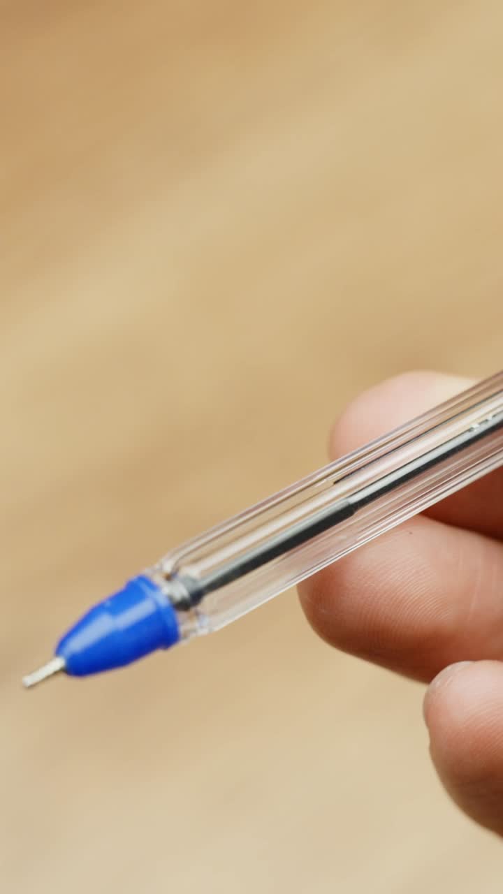 Hand holding a transparent blue pen in focus, indoor close-up with soft background